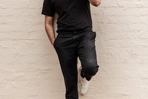 man in black crew neck t-shirt and blue denim jeans leaning on white wall