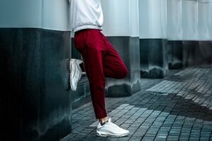 man in white long sleeve shirt and red pants leaning on wall