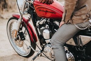 man sits on red and black Harley-Davidson motorcycle during daytime