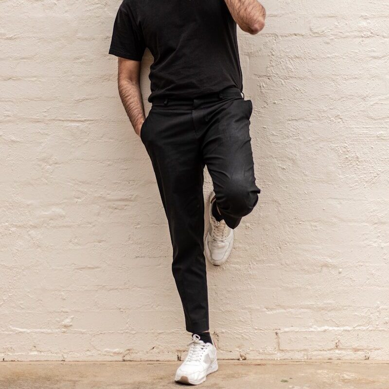 man in black crew neck t-shirt and blue denim jeans leaning on white wall