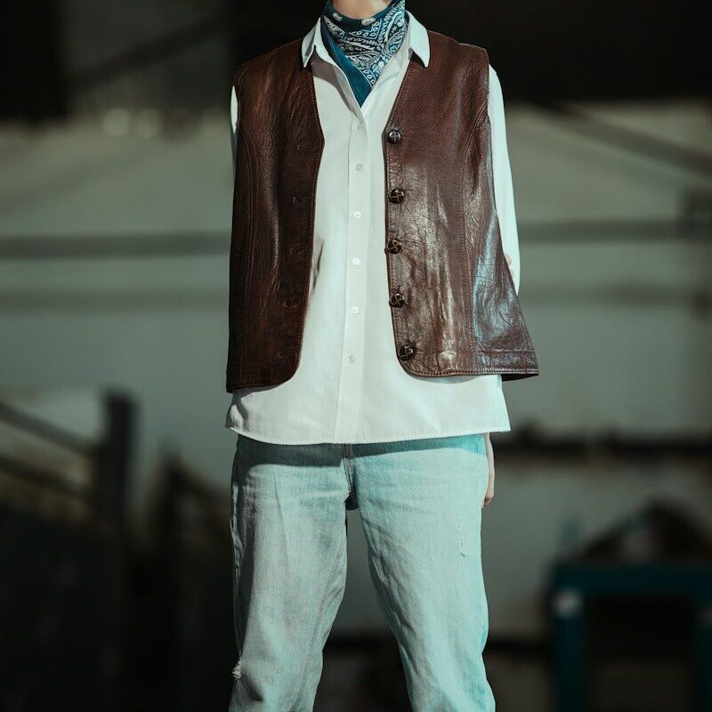 Young person in a vest and bandana looks away