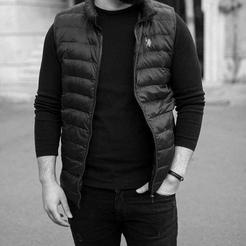 man in black jacket and black pants standing on sidewalk in grayscale photography