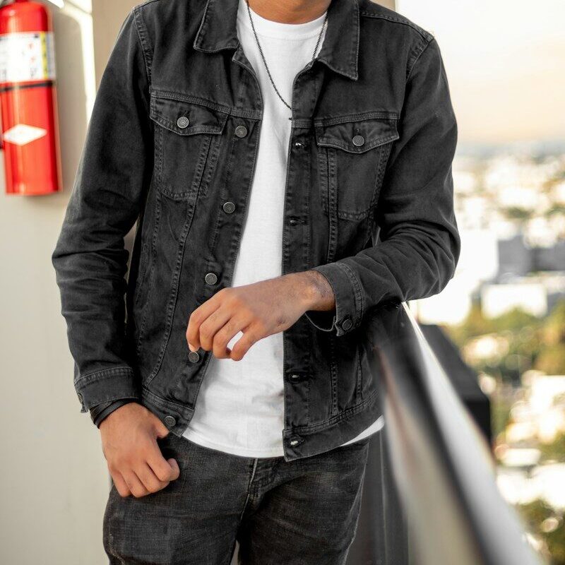 man in black leather jacket standing near white wall